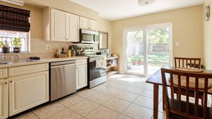 A kitchen with white cabinets, a dishwasher, an oven, and a microwave. There is a dining table with chairs and a window with blinds. - Inviting home w/ big yard & walkable neighborhood! 3br/2ba (Tampa)