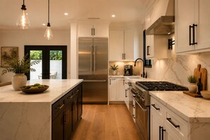 Una cocina moderna con una isla grande, electrodomésticos de acero inoxidable e iluminación colgante.