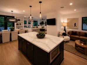 A modern kitchen with a marble island, dark cabinetry, pendant lighting, and a view of the living area. - Gated Santa Barbara Villa, Walk to Hendry's Beach, with Private Casita (Santa Barbara)