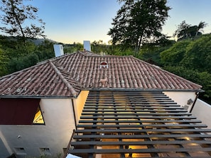 A house with a tiled roof, a wooden deck, and a view of the surrounding greenery.