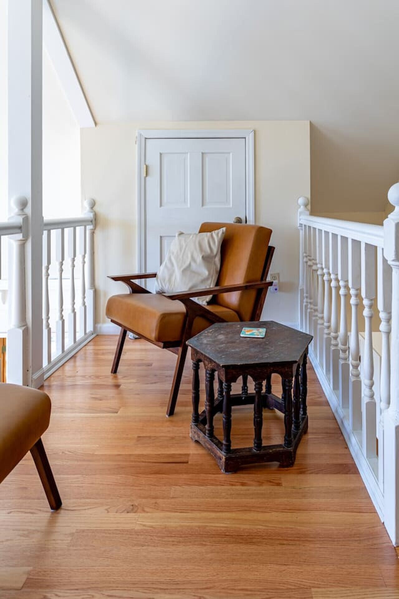 Un balcon au plancher de bois, avec une balustrade blanche, un fauteuil en cuir marron, une petite table et, au fond, une porte blanche.