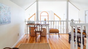 A spacious room with a wooden floor, a white railing, a table with chairs, and a hanging light fixture.