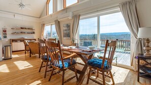 A spacious dining area with a wooden table and chairs, large windows offering a view of the outdoors, and a balcony with a railing.