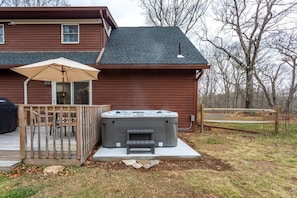 A wooden deck with a hot tub, a covered patio table, and chairs.