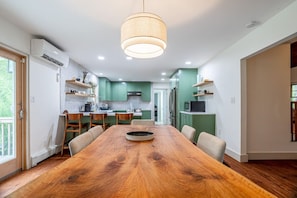 Une cuisine moderne avec des meubles de couleur verte, une table à manger en bois et un luminaire suspendu.