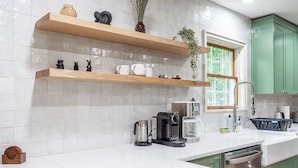 A modern kitchen with white marble countertops, wooden shelves, and green cabinets.