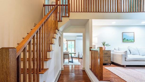 A modern interior with a wooden staircase leading to a dining area and a living room with a sofa and a painting.