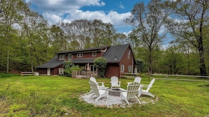 A two-story wooden house with a fenced yard, a fire pit, and Adirondack chairs.