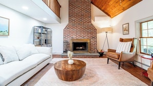 A living room with a brick fireplace, white sofa, and a wooden coffee table.