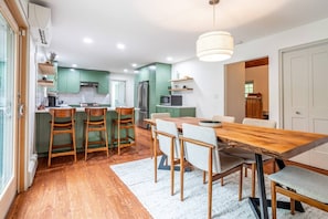 A modern kitchen with green cabinets, a wooden dining table, and a hanging light fixture.