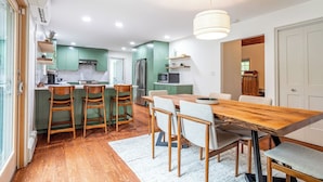 A modern kitchen with green cabinets, a wooden dining table, and a white ceiling light.