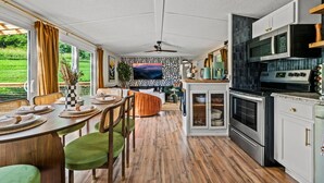 A modern kitchen with a dining area, large windows, and a view of greenery.