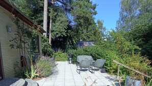 A patio area with a barbecue grill, outdoor furniture, and a variety of plants.