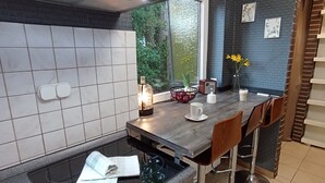 A modern kitchen with a black countertop, white tiles, a window with a view of greenery, and a bar area with stools.