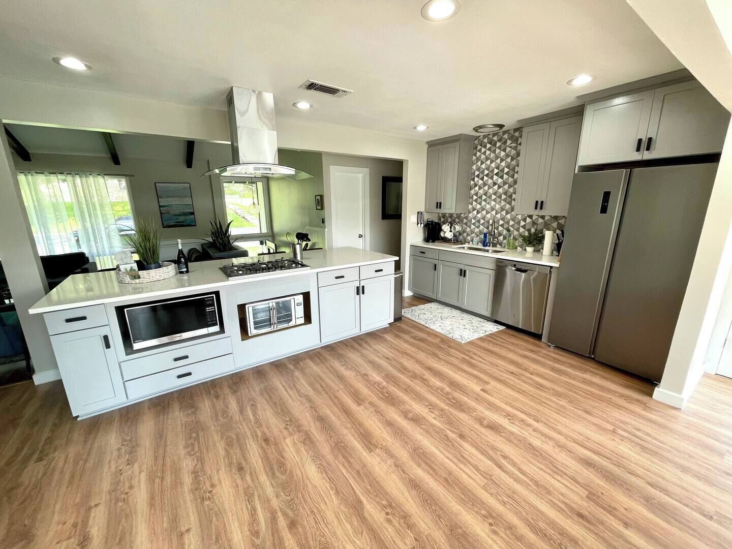 A modern kitchen with a central island, built-in appliances, and a large window providing natural light.