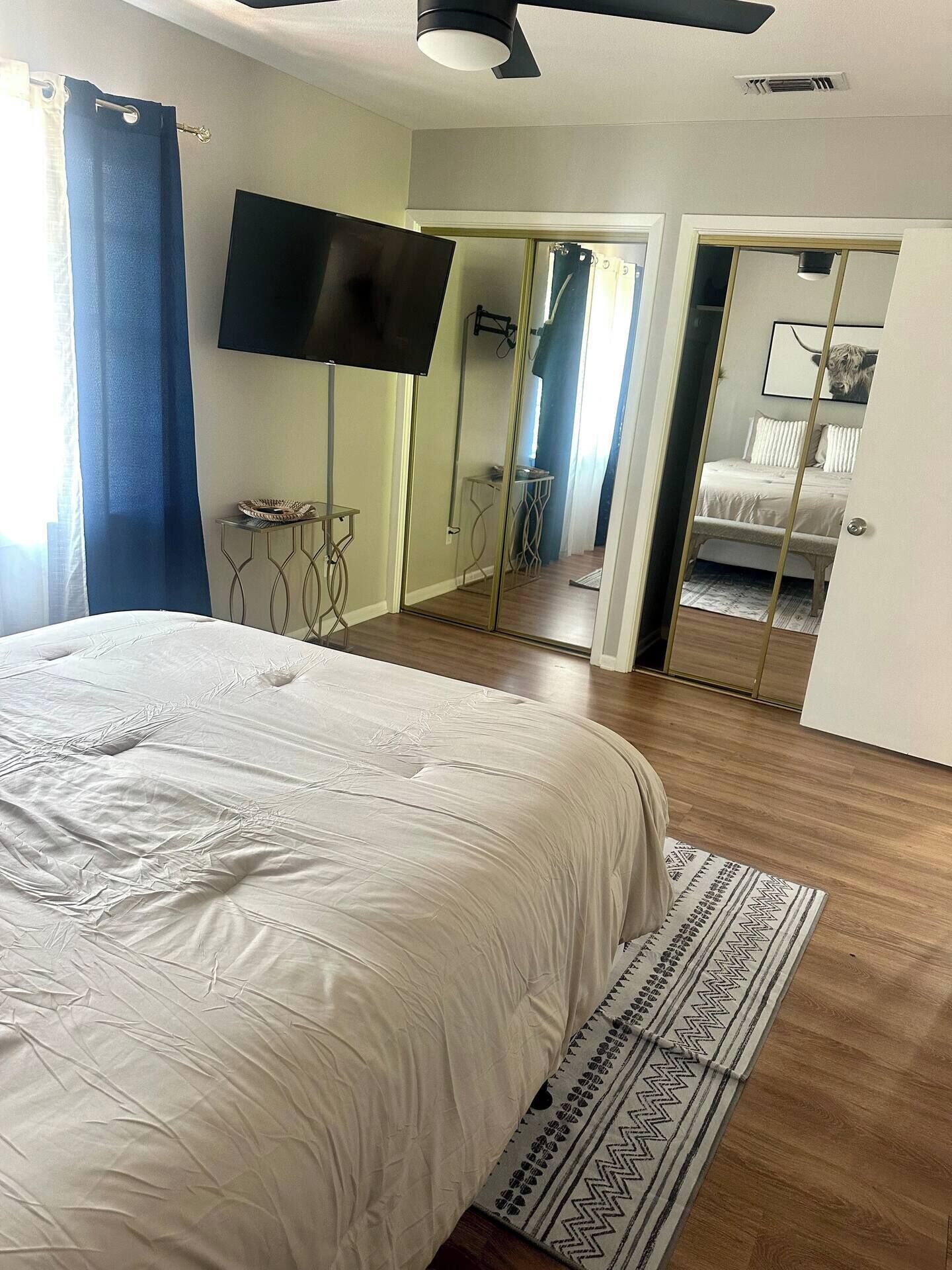 Une chambre à coucher avec un lit, un téléviseur fixé au mur, un miroir et une porte donnant sur une autre pièce.