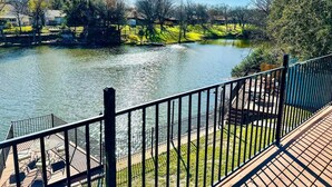 Terraza junto al río con barandilla de madera, una mesa pequeña con sillas y vistas a un río tranquilo y vegetación circundante.