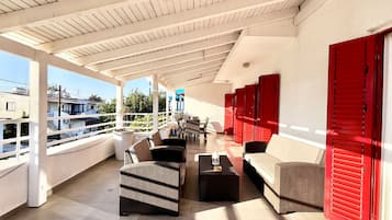 A covered outdoor seating area with wicker furniture and red shutters.