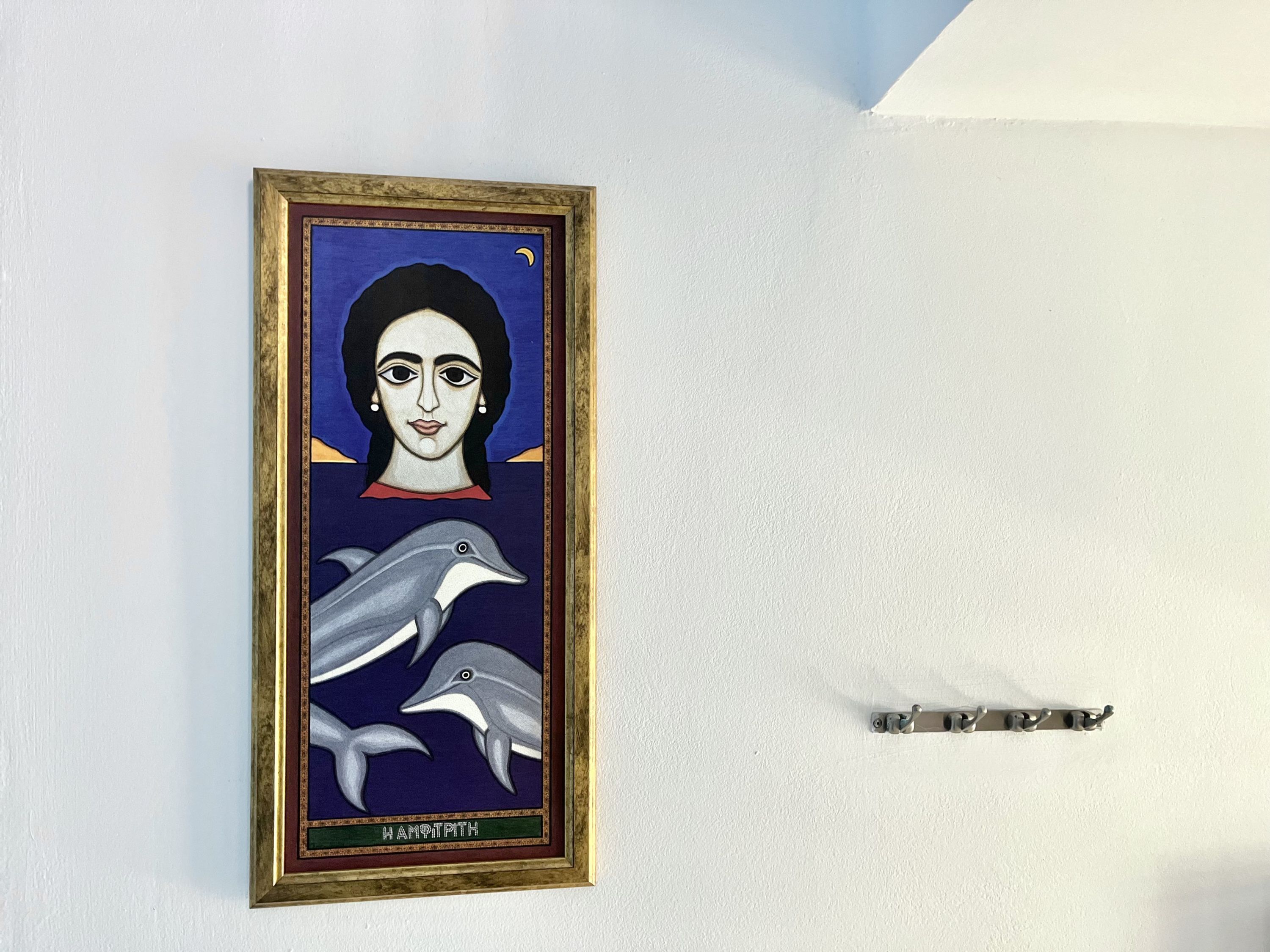 Une œuvre d’art encadrée représentant une femme et des dauphins sur un mur blanc.