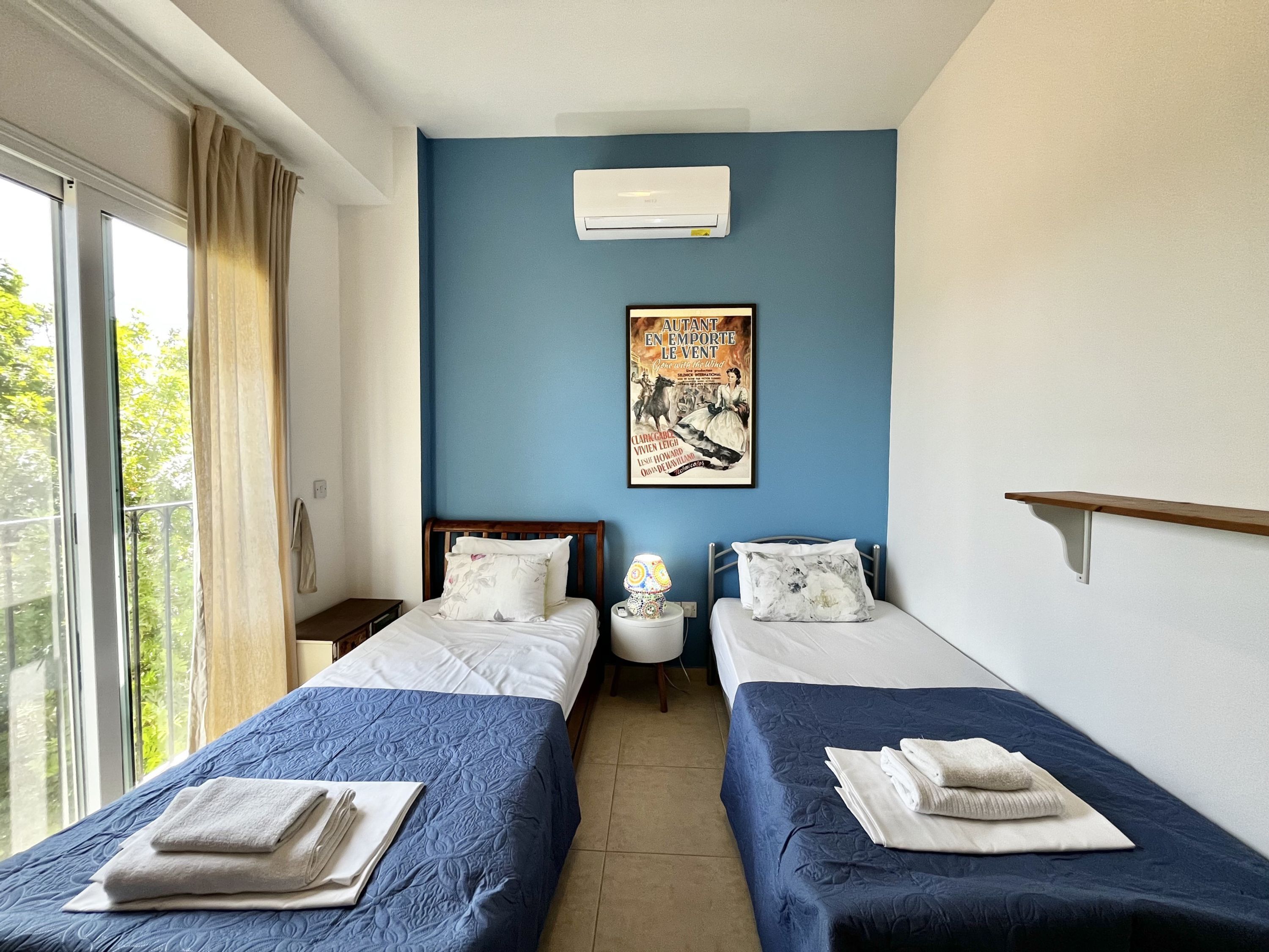 A hotel room with two beds, a window with curtains, an air conditioner, and a poster on the wall.