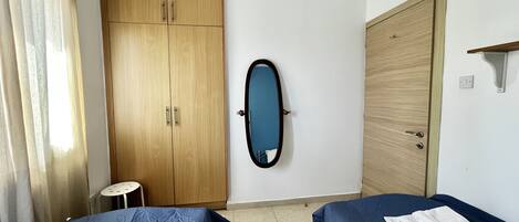 Una habitación con dos camas, un armario de madera, un espejo y un taburete pequeño.