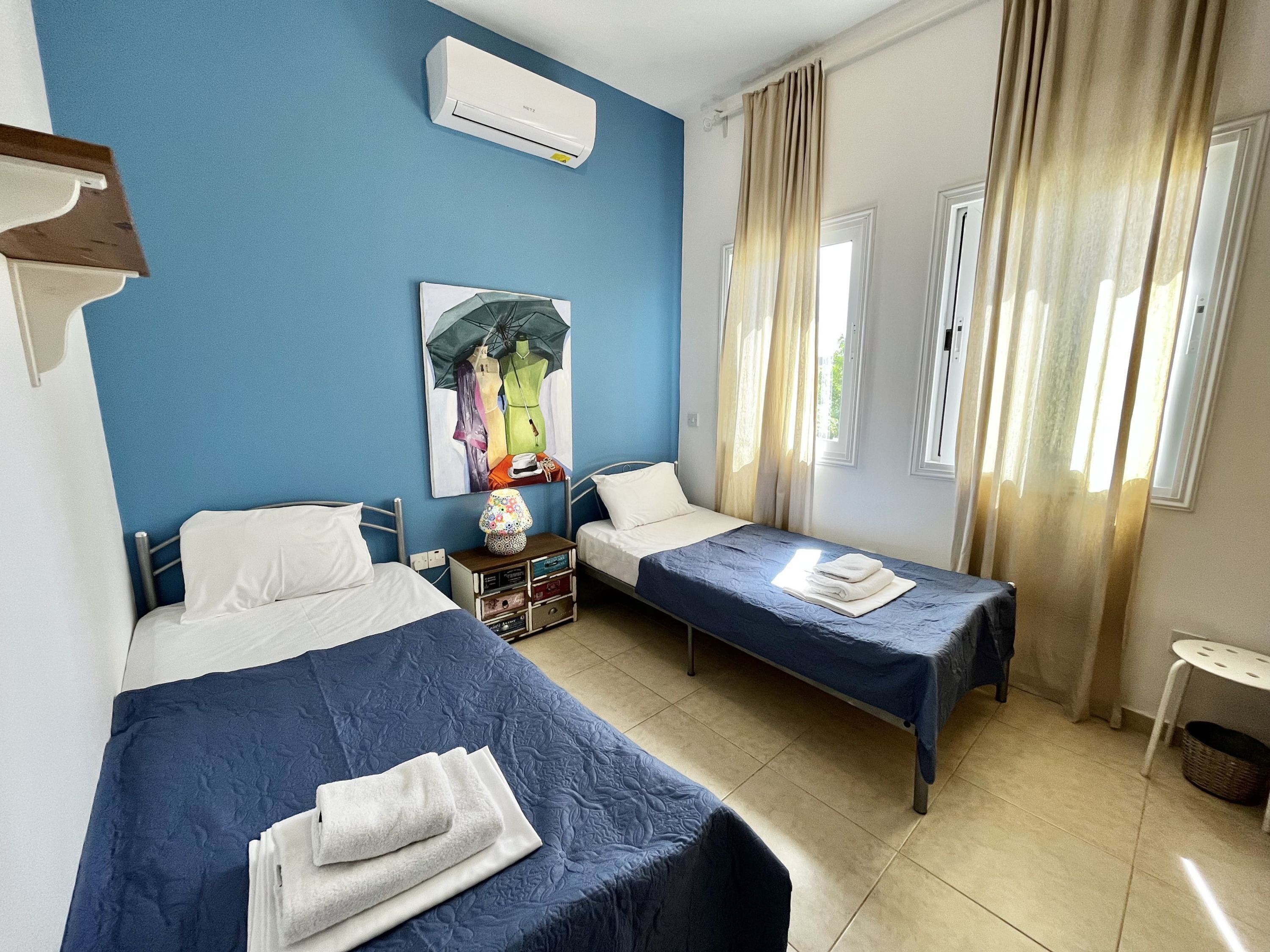 Una habitación con dos camas, aire acondicionado instalado en la pared, un cuadro y una ventana con cortinas.