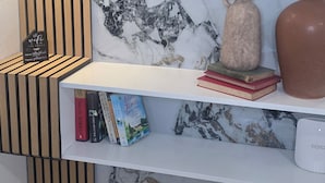 Ein modernes Interieur mit Marmorwand, Holzlamellen und Regalen mit Büchern und Dekoration.
