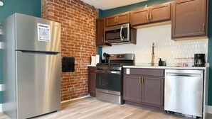 A modern kitchen with stainless steel appliances, wooden cabinets, and a brick accent wall.