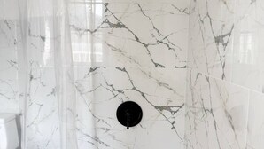 A bathroom with a white marble wall, a bathtub, and a shower with a circular head.