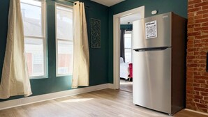 A kitchen with a stainless steel refrigerator, a window with curtains, and a view of a red chair in the background.