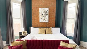 A bedroom with a large bed, a red upholstered sofa, and a brick wall.