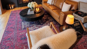A cozy living room with a leather sofa, a coffee table with candles, a fireplace, and a mounted television.
