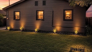 A two-story house with a dark siding exterior, three windows, and a small front yard with plants.