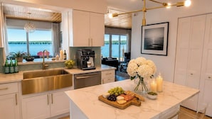 A modern kitchen with a large island, a coffee machine, and a view of the outdoors.