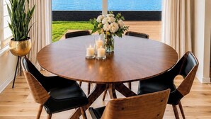 A round wooden table with chairs, a chandelier, and a view of a lake.