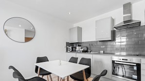 Una cocina moderna con una mesa blanca y sillas negras, un horno empotrado y una campana extractora de acero inoxidable.