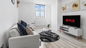 Una sala de estar moderna con un sofá blanco, una mesa de centro, un televisor sobre un mueble blanco y obras de arte en la pared.