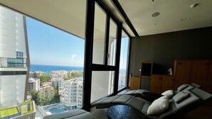 A modern living room with a large window, a sofa, a small table, and a wooden cabinet.