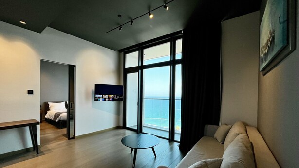 A modern living room with a large window, a flat-screen TV, a sofa, and a small round table.