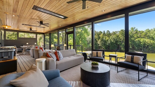 Ein geräumiger Wohnbereich mit großem Sofa, Couchtisch und Sitzgelegenheiten an einem großen Fenster mit Blick auf einen Wald.