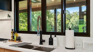 Eine Küche mit einem großen Fenster, einem modernen Wasserhahn und verschiedenen Küchenutensilien auf der Arbeitsplatte.