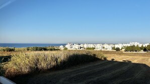 Vista costera con edificios blancos, cielo despejado y un campo en primer plano.