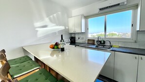 Una cocina moderna con una isla grande, armarios blancos, un ventanal con vistas a la ciudad y asientos acolchados verdes.