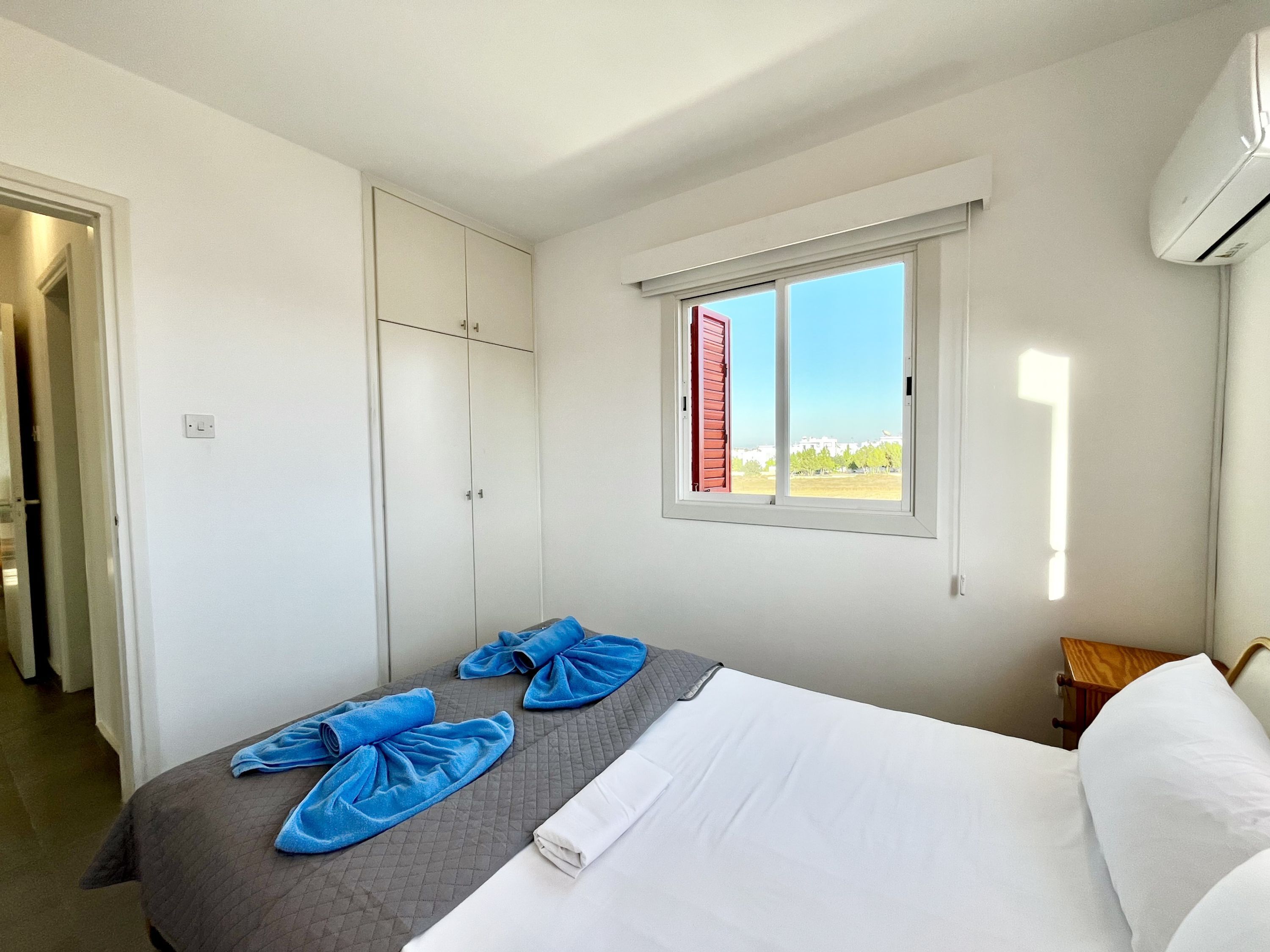 A hotel room with a bed, a wardrobe, a window with a view, and an air conditioning unit.