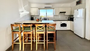 Una cocina moderna con una isla central, sillas de madera, un refrigerador y una ventana con vistas.