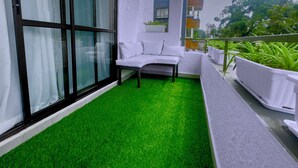 Uma varanda com grama sintética verde, um sofá branco e plantas em vasos.