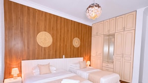 Quarto duplo com duas camas, painéis de madeira nas paredes, um candelabro e um guarda-roupa.