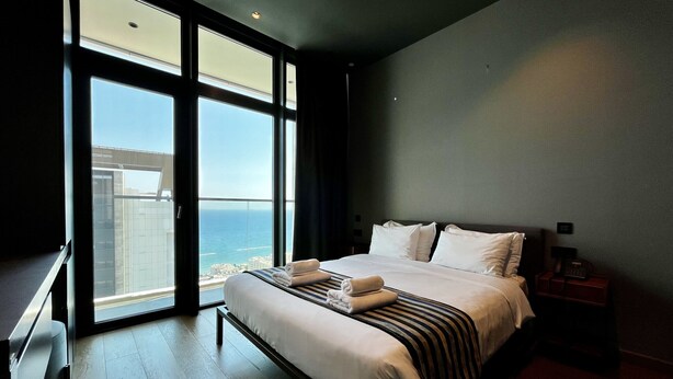 A modern hotel room with a large bed, a desk, and a view of the ocean.