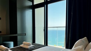 A hotel room with a bed, a window with a view of the sea, and a small table with towels.