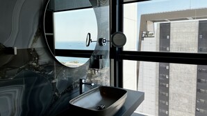A modern bathroom with a large window, a round mirror, and a vessel sink.
